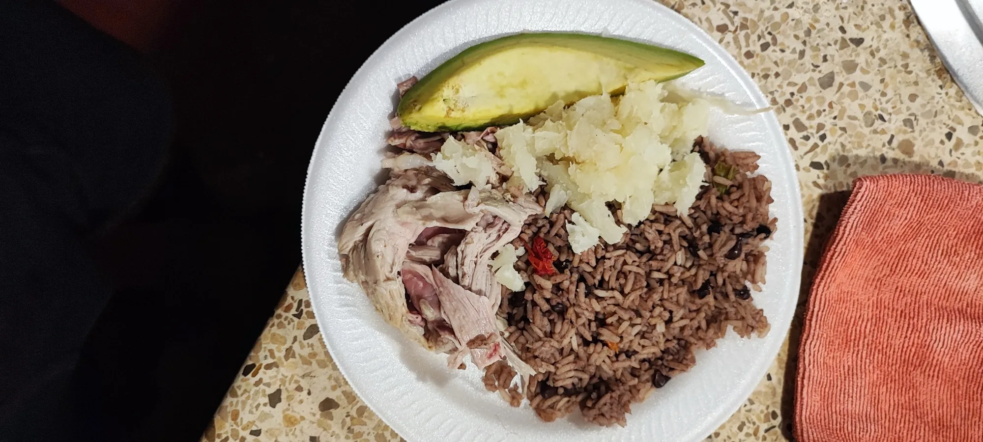 Plato blanco con carne deshebrada, arroz con frijoles negros, yuca y un trozo de aguacate
