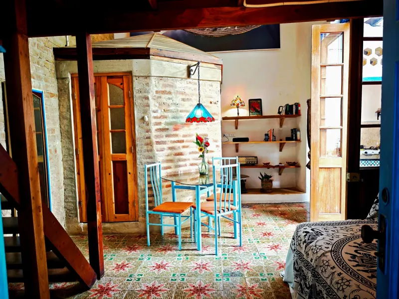 Salon avec une table en verre, des chaises turquoise et un escalier en bois